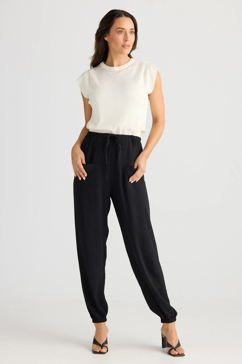 Woman wearing a white sleeveless top and black pants on a white background