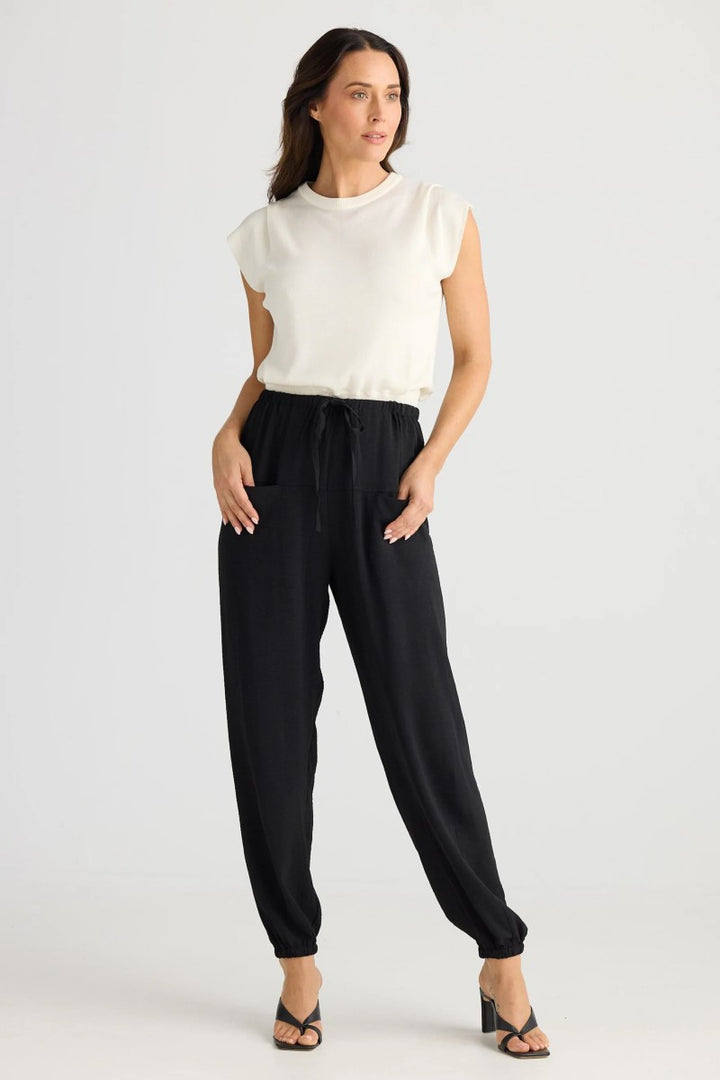 Woman wearing a white sleeveless top and black pants on a white background