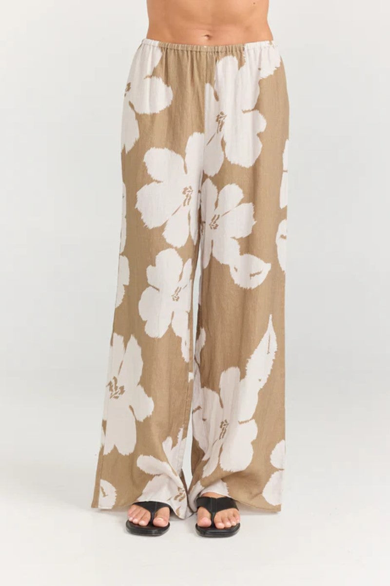 Beige pants with white floral pattern worn by a person on a white background