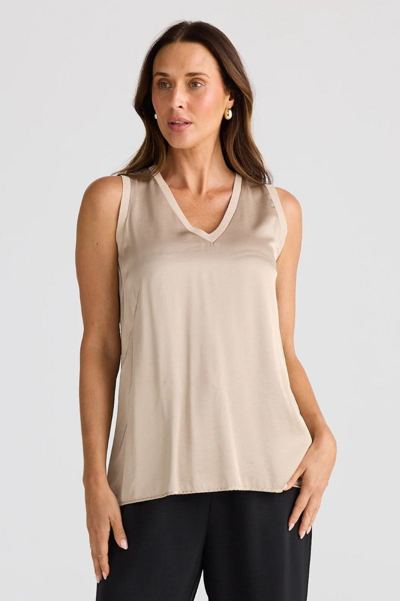 Woman wearing a beige sleeveless top against a plain background