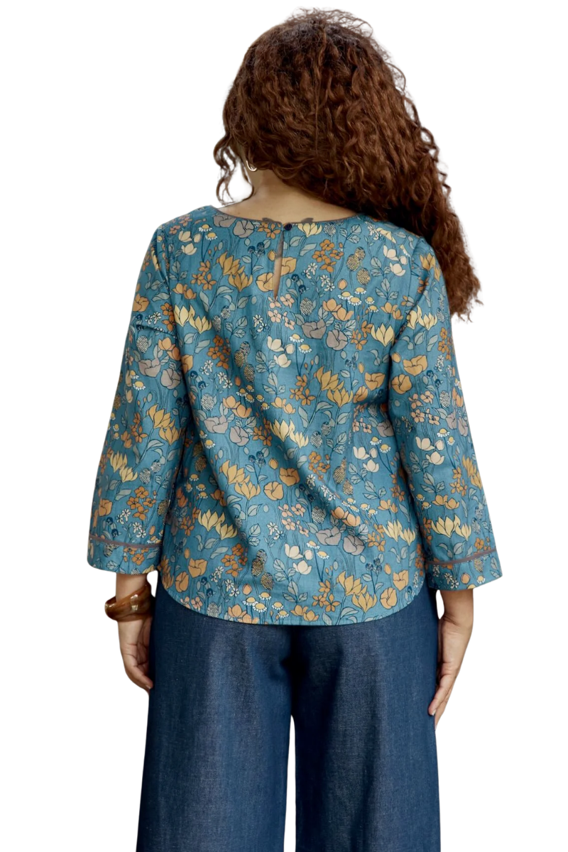 Woman wearing a blue floral blouse and dark pants on a white background