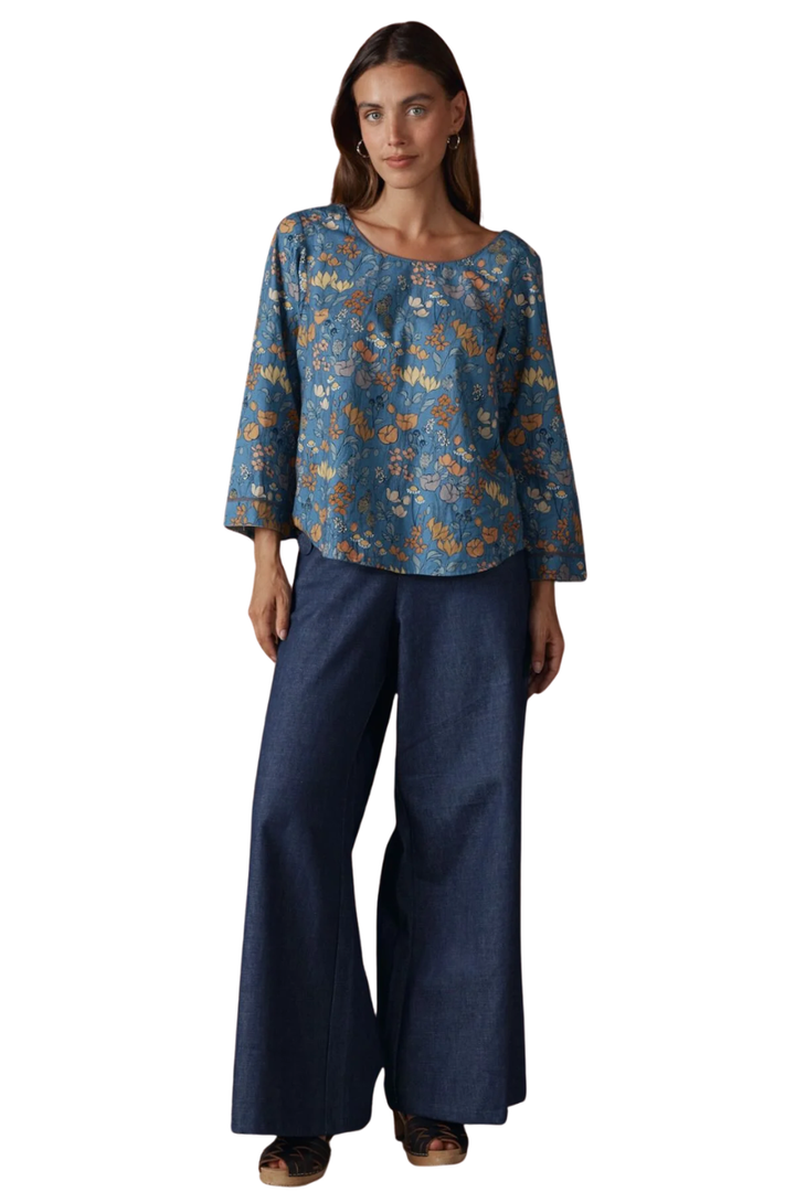 Woman wearing a blue floral blouse and dark blue pants on a white background