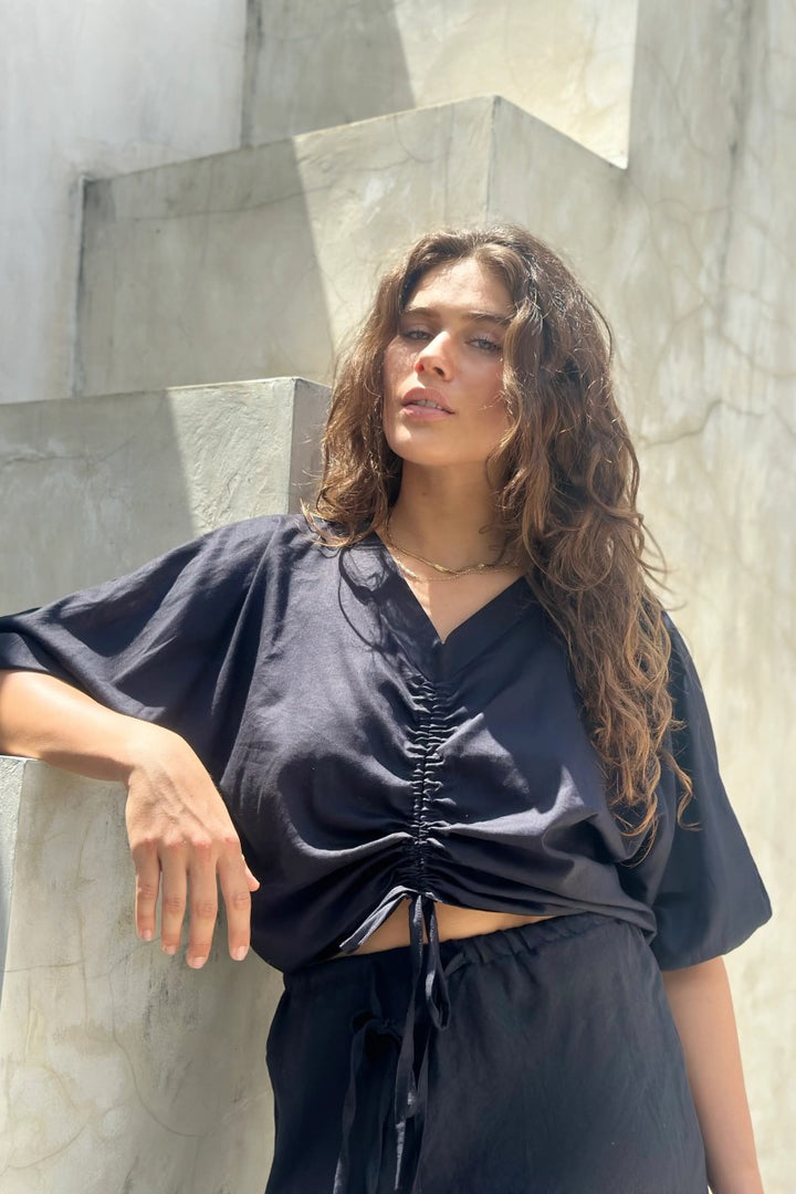 Woman wearing a black outfit standing against a stone wall.