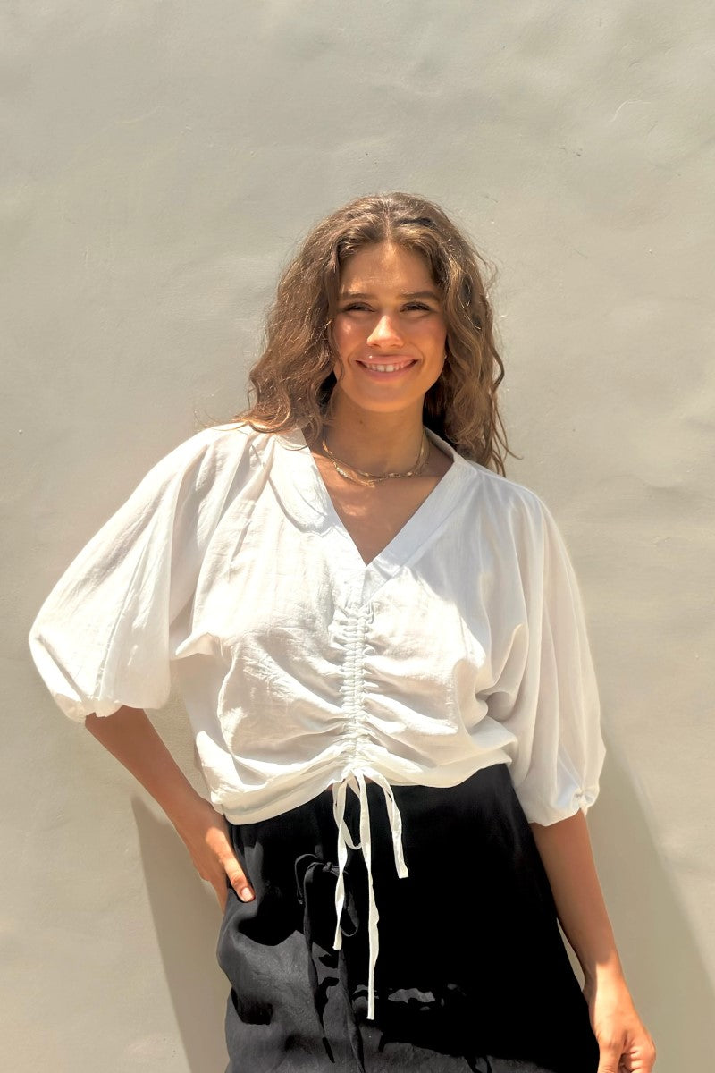 Woman wearing a white blouse with balloon sleeves against a plain background