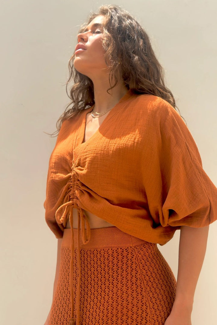 Woman wearing an orange top and skirt against a plain background