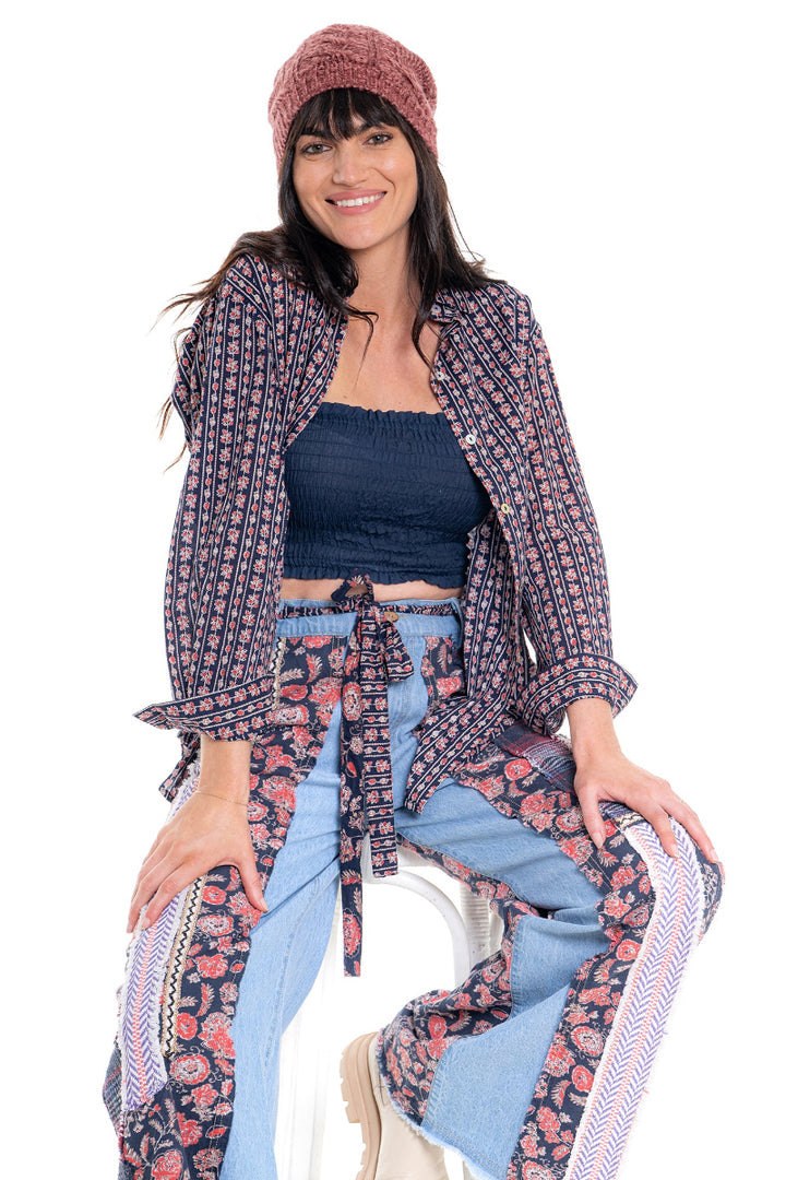 Woman wearing a patterned jacket, blue top, and light blue jeans on a white background