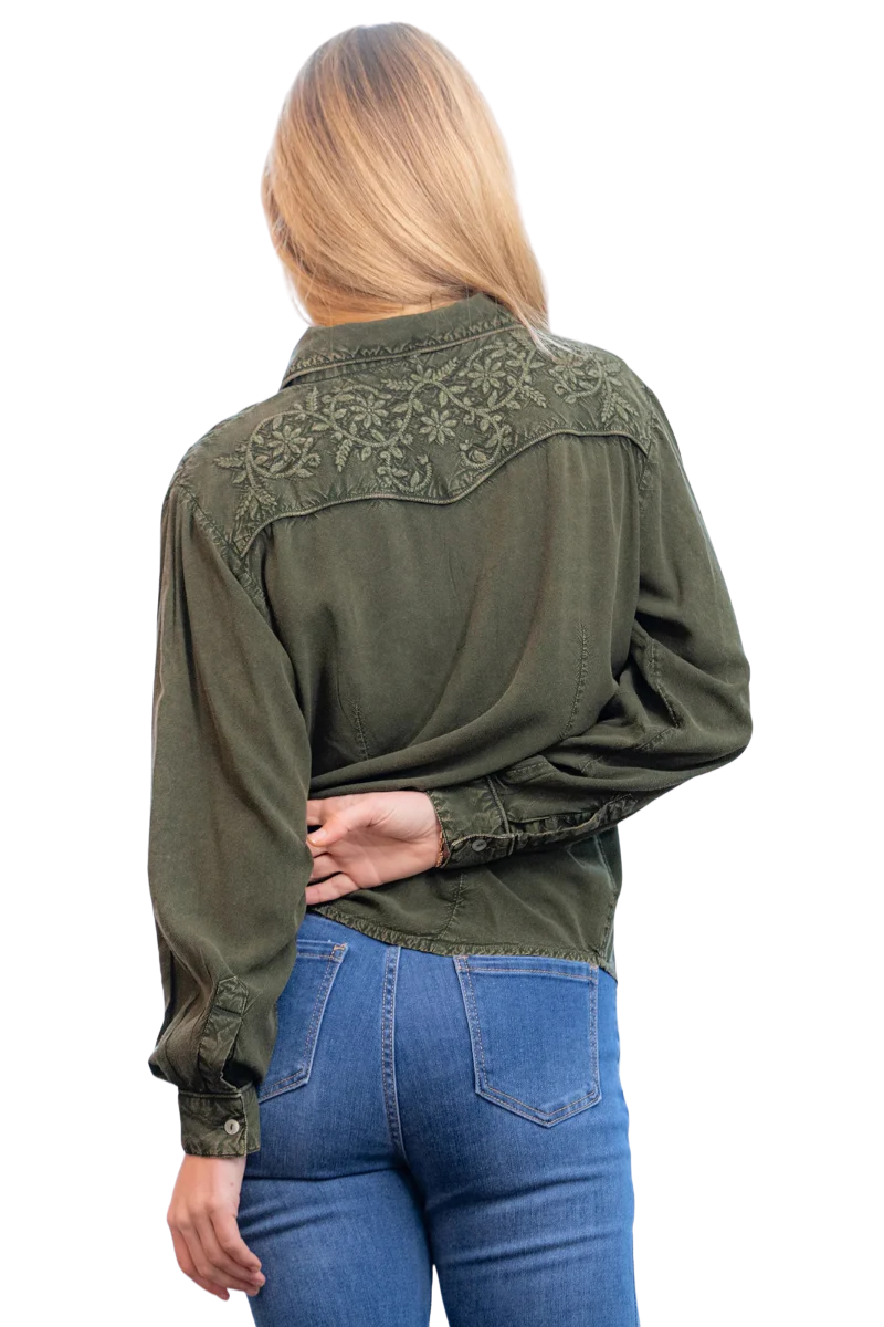 Person wearing an olive green embroidered shirt and blue jeans on a white background