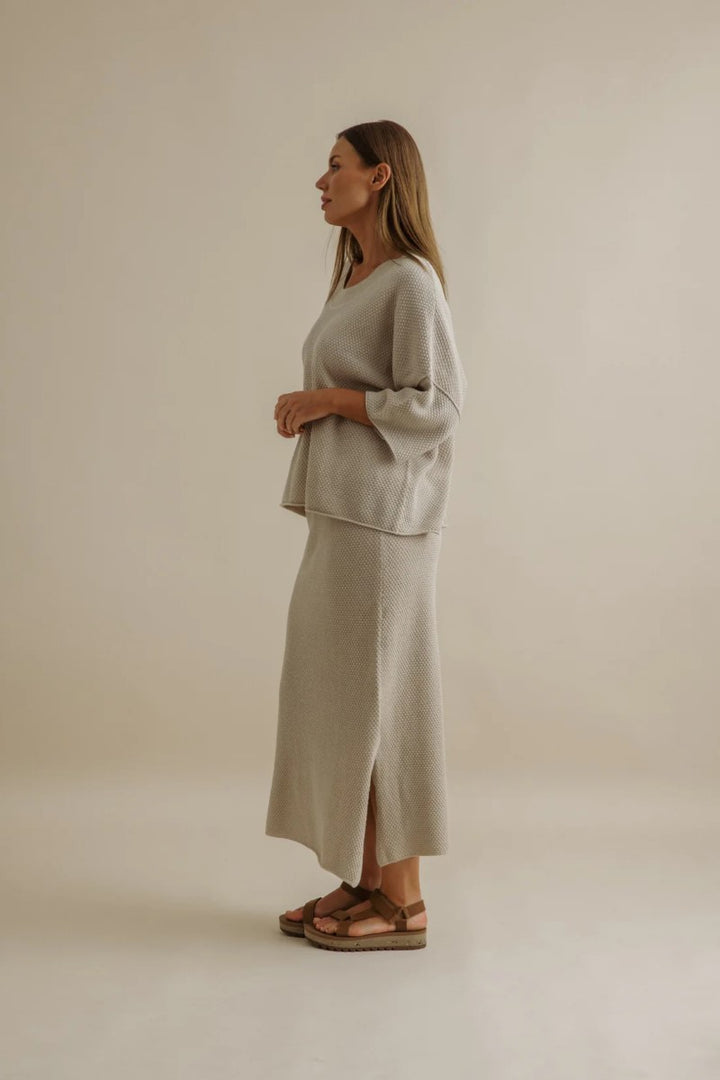 Woman wearing a light gray outfit standing against a plain background