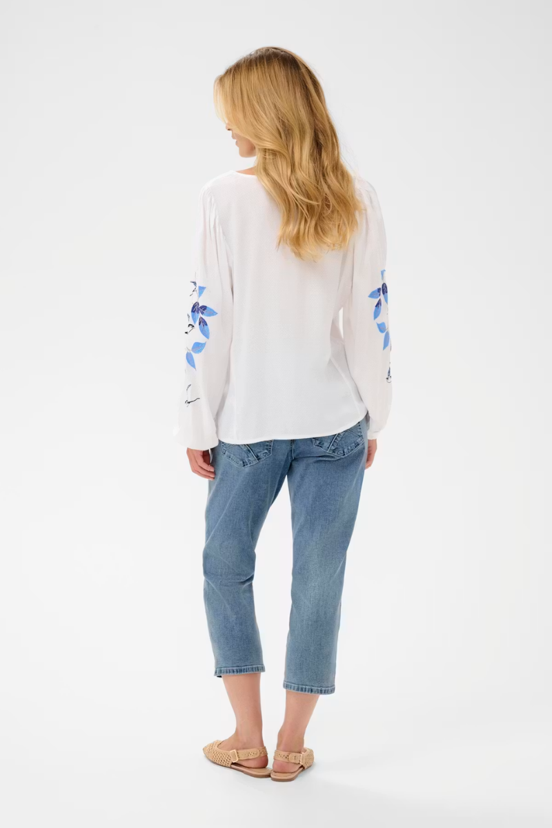Woman wearing a white long-sleeve shirt with blue floral patterns and blue jeans on a white background