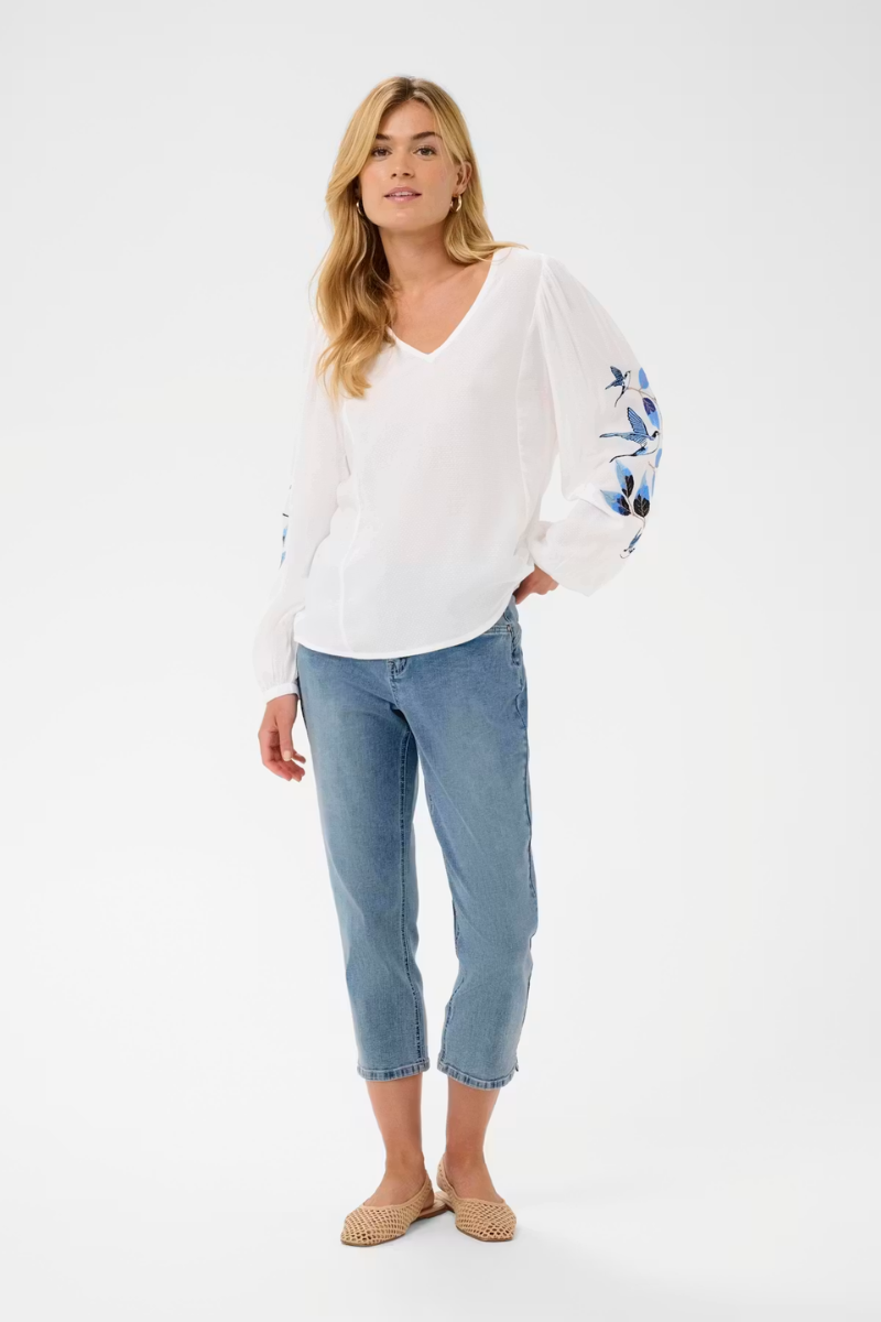 Woman wearing a white blouse with floral embroidery and light blue jeans on a white background