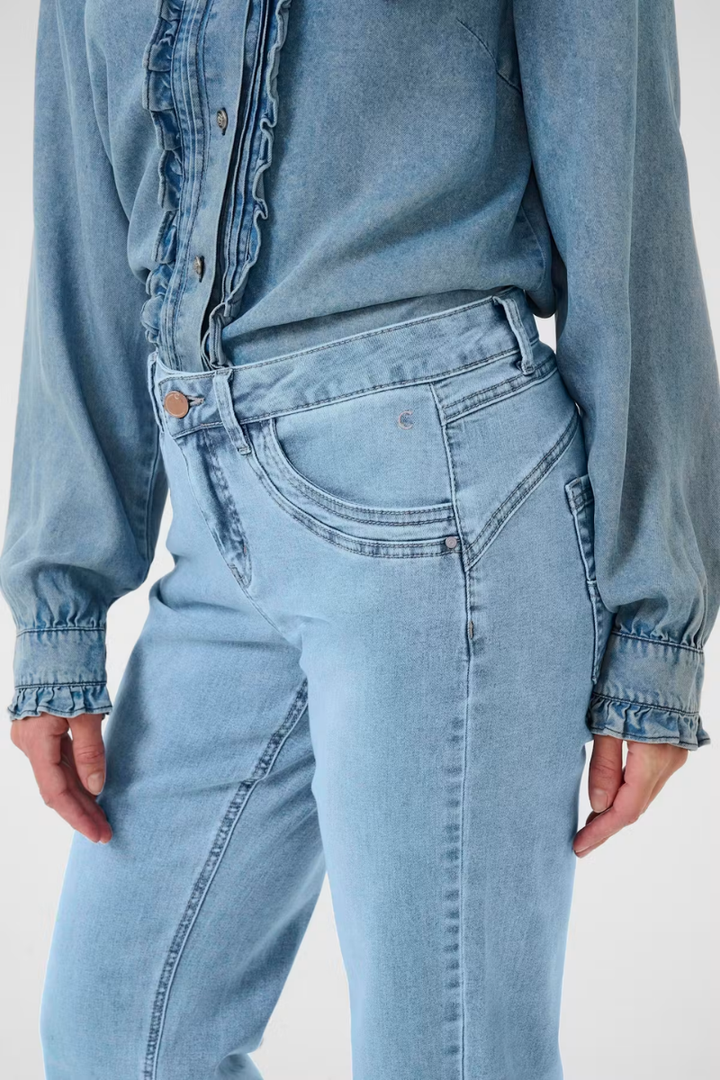 Person wearing a light blue denim shirt and jeans on a plain background