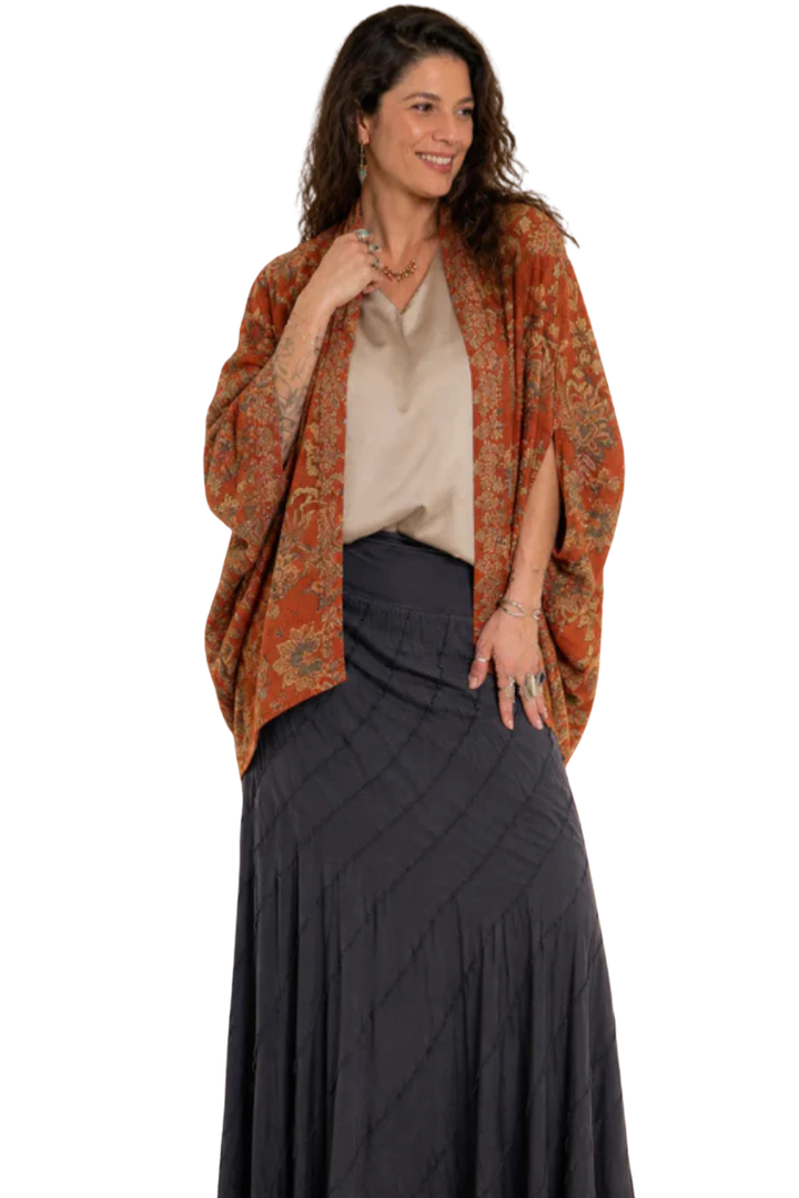 Woman wearing a patterned orange jacket over a white shirt and dark skirt on a white background