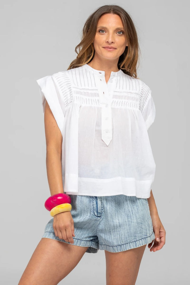 Woman wearing a white sleeveless blouse and denim shorts on a gray background