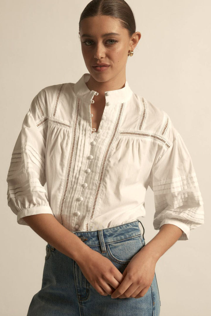 White textured blouse with short puff sleeves, delicate lace trim panels, and a row of buttons down front, slightly gathered fit. 