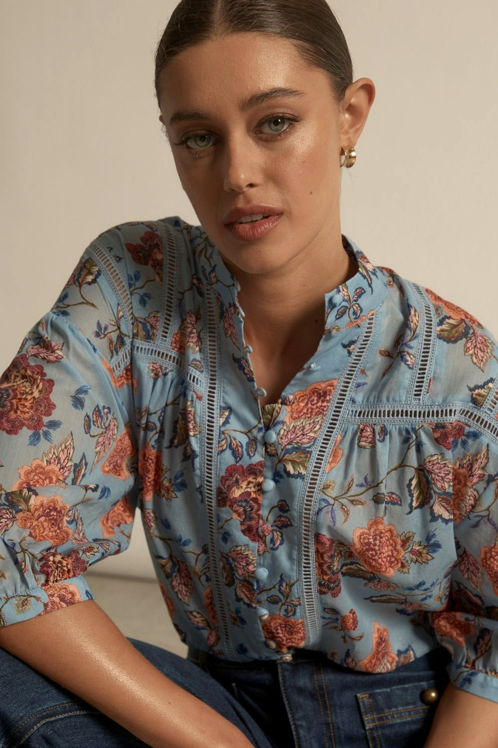 Woman wearing a floral blouse with blue, orange and green accents.