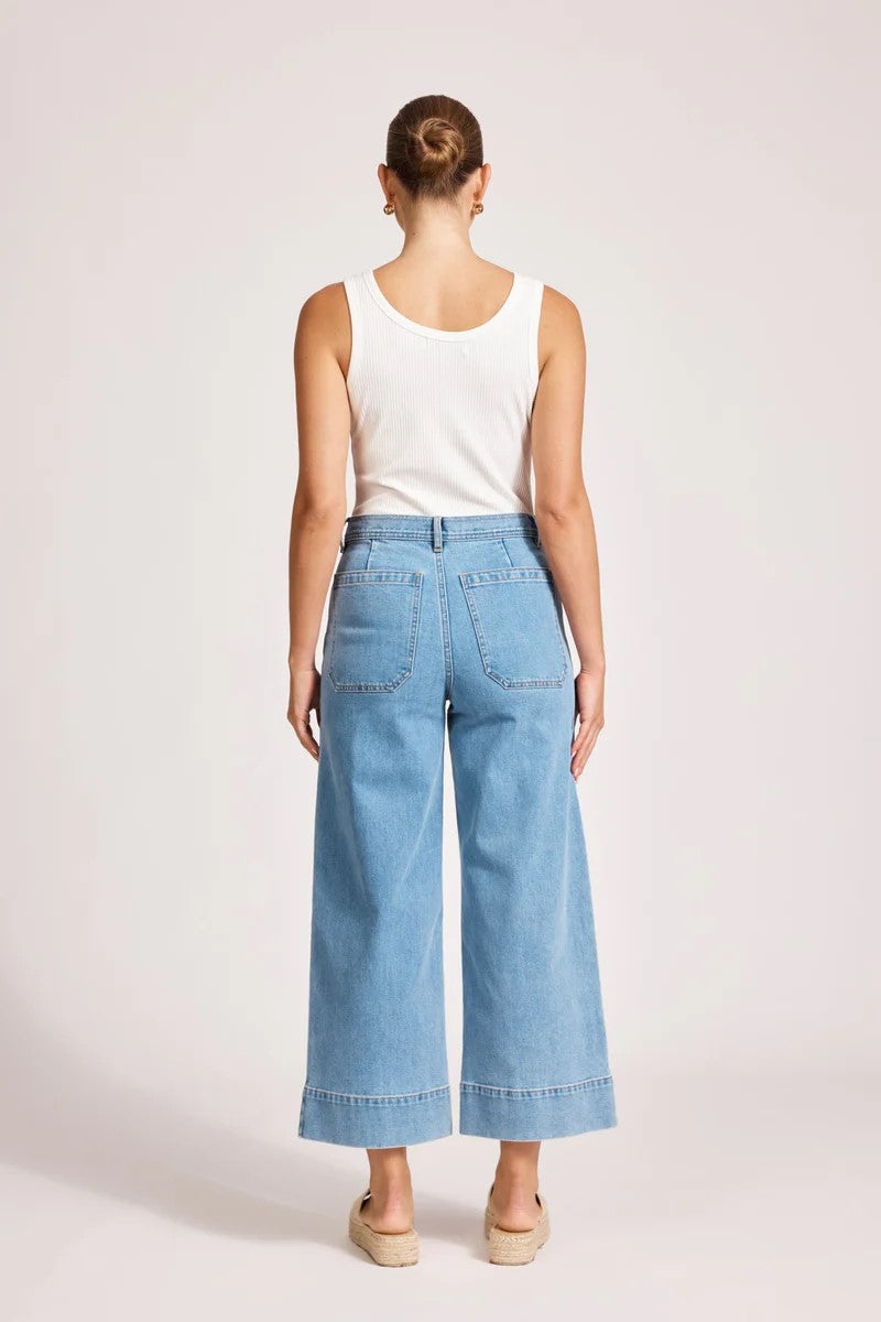 Person wearing light blue jeans and a white top on a plain background