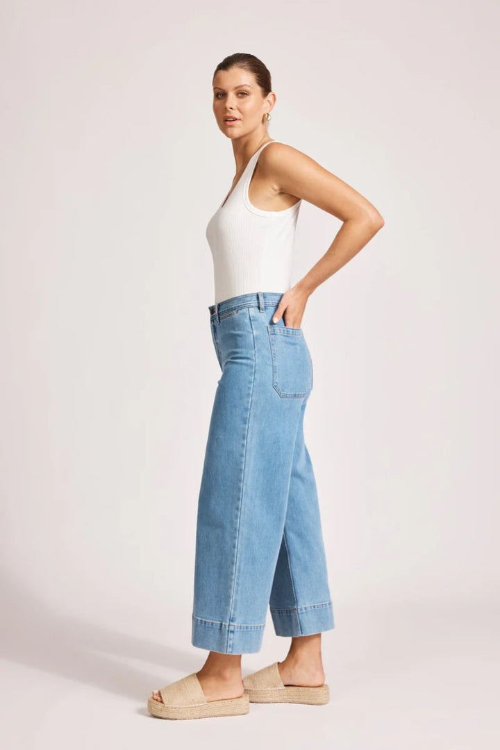 Woman wearing a white top and blue jeans on a light pink background