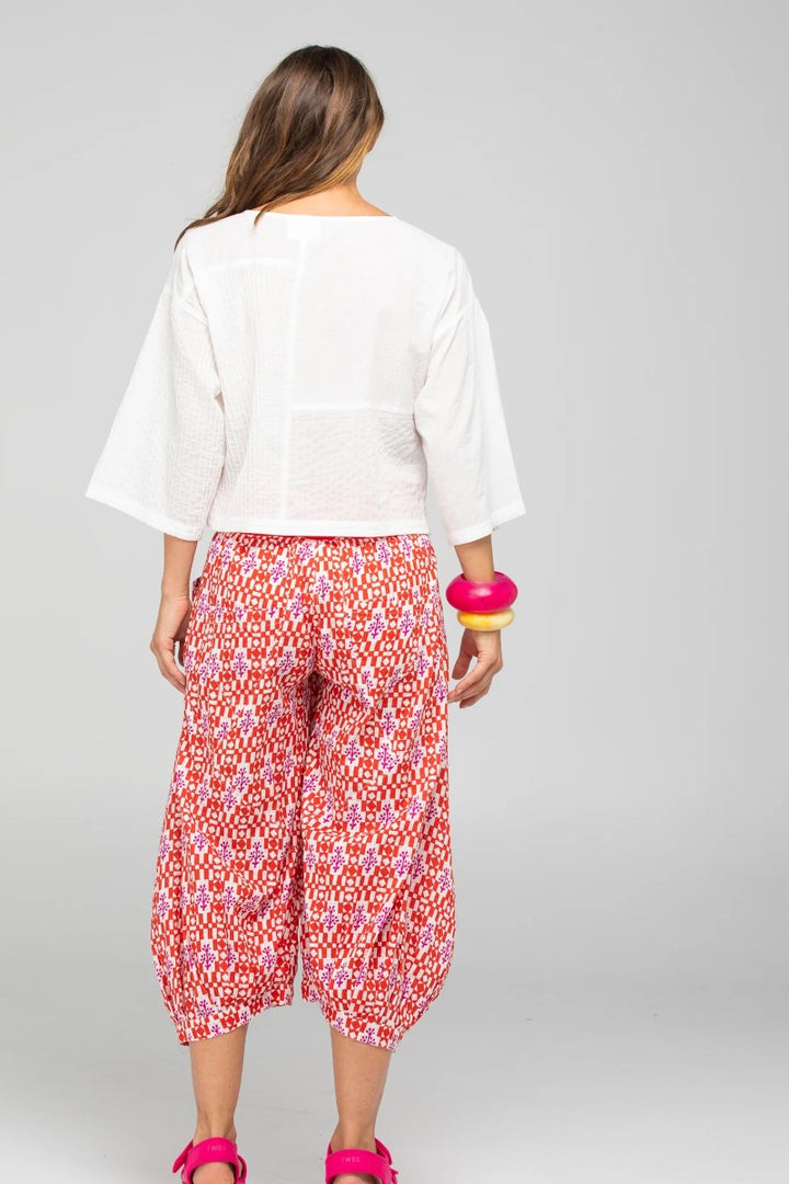 Woman wearing a white top and red floral pants on a gray background