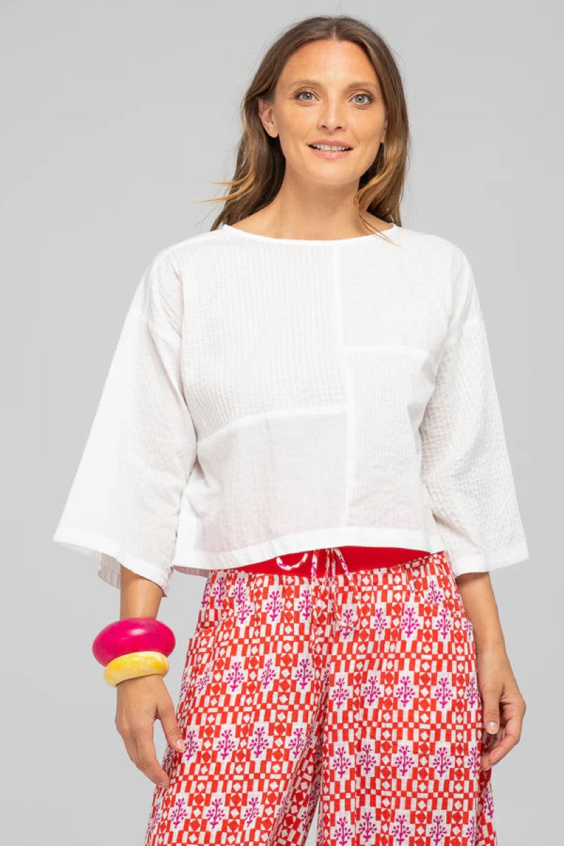 Woman wearing a white top and red patterned pants on a gray background