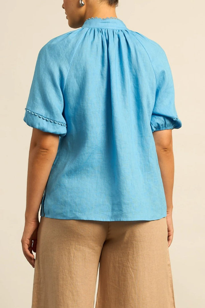 Person wearing a blue top with short sleeves and brown pants on a beige background