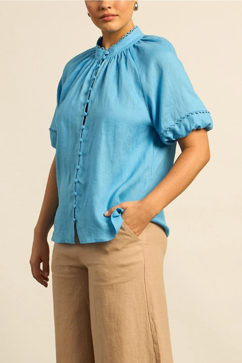 Person wearing a blue blouse with short sleeves and beige pants on a beige background