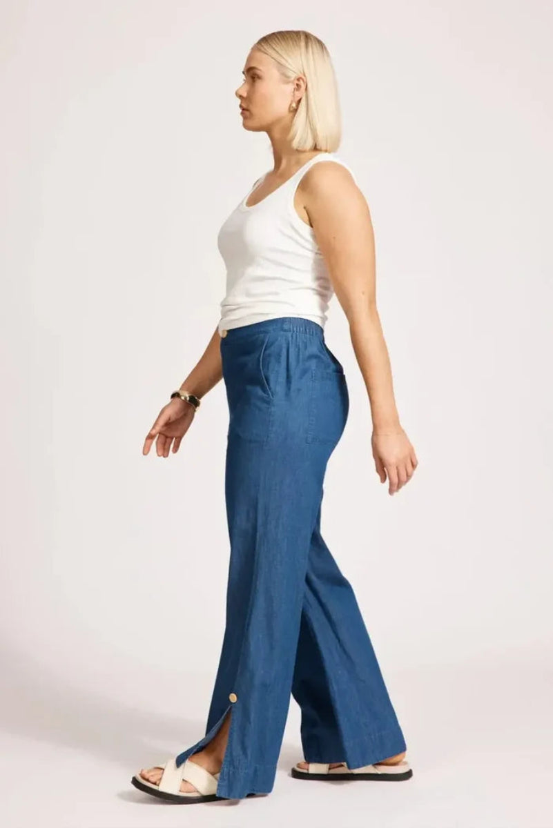 Woman wearing blue wide-leg pants and a white top on a plain background