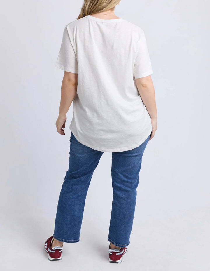 Back view of beige graphic T-shirt with jeans and sneakers.
