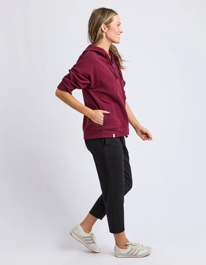 Woman wearing a burgundy hoodie and black pants on a white background