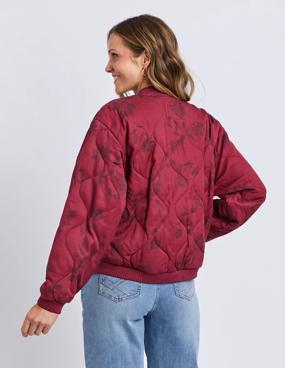 Person wearing a red quilted jacket with floral patterns on a plain background
