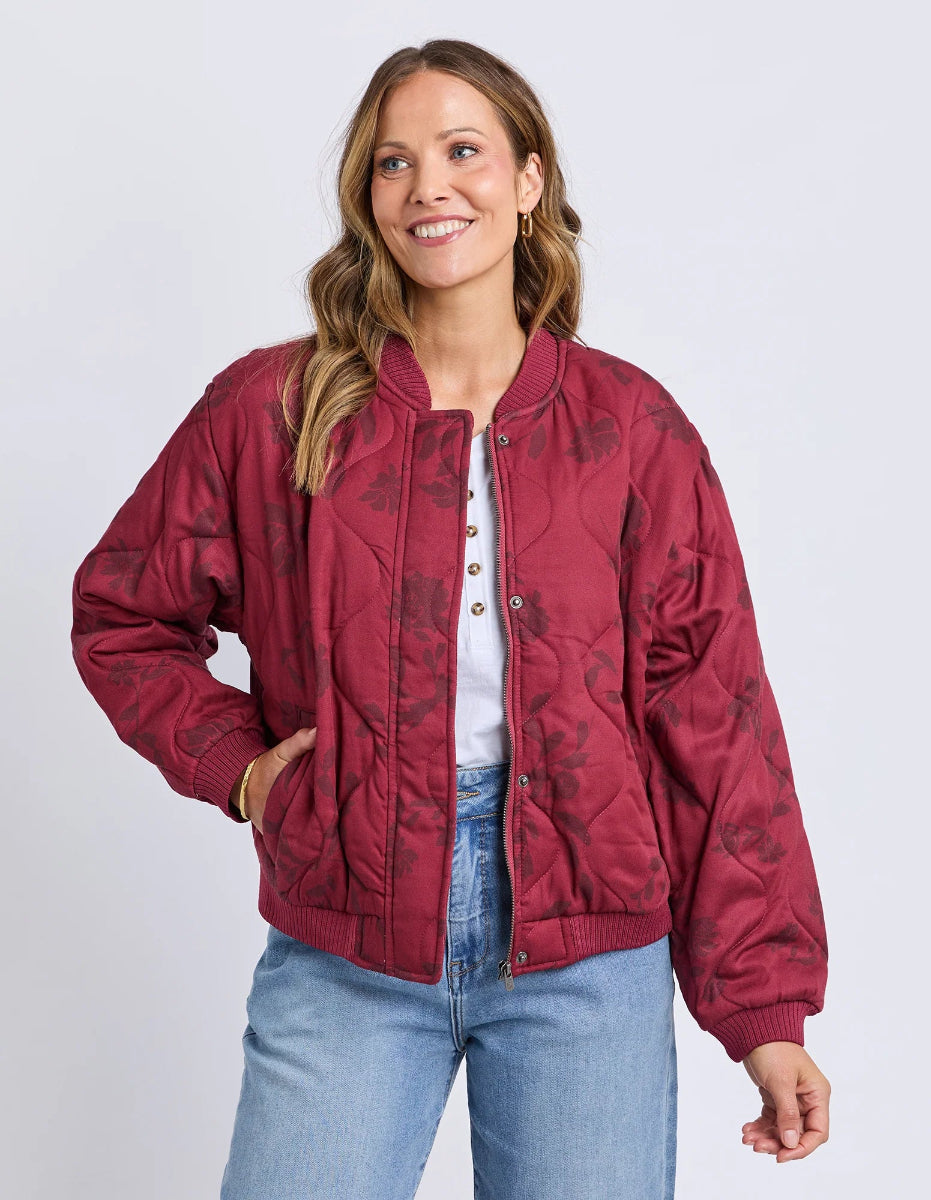 Woman wearing a red quilted jacket with floral patterns on a plain background