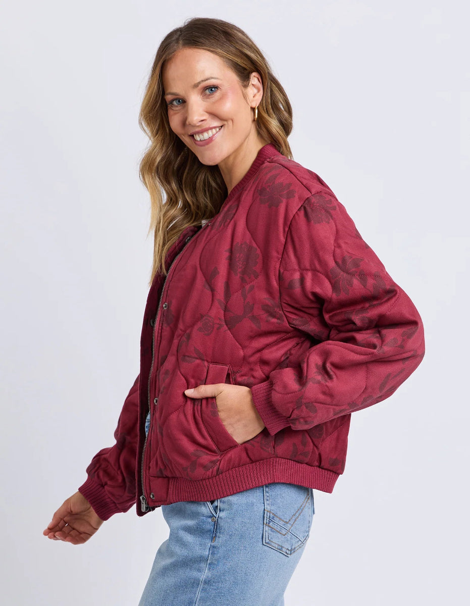 Woman wearing a red bomber jacket with a subtle pattern on a white background