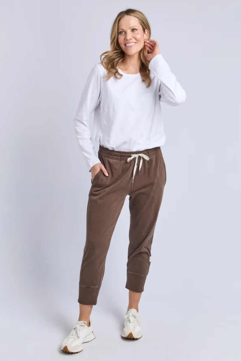 Woman wearing a white long-sleeve top and brown pants on a light gray background