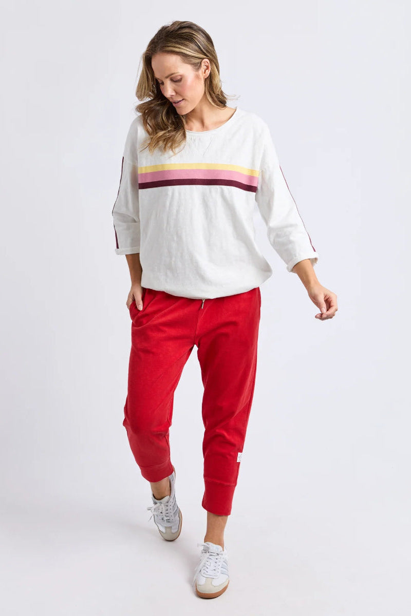 Front view of red cropped jogger pants styled with white long-sleeve top.