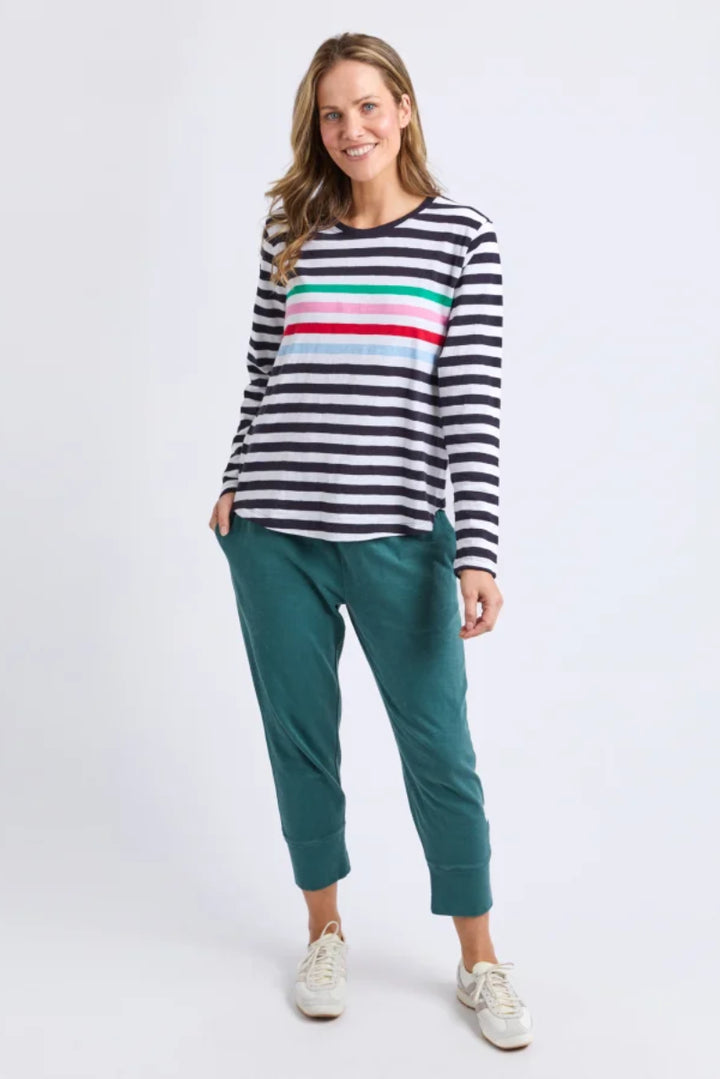 Woman wearing a striped sweater with colorful horizontal stripes and green pants on a white background