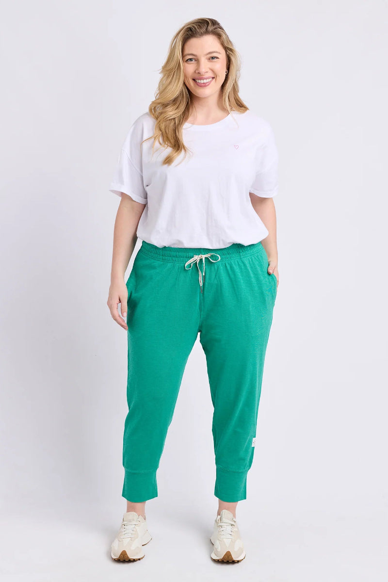 A woman modeling bright green jogger pants with a white drawstring, styled with a white t-shirt and white sneakers against a light gray studio background.