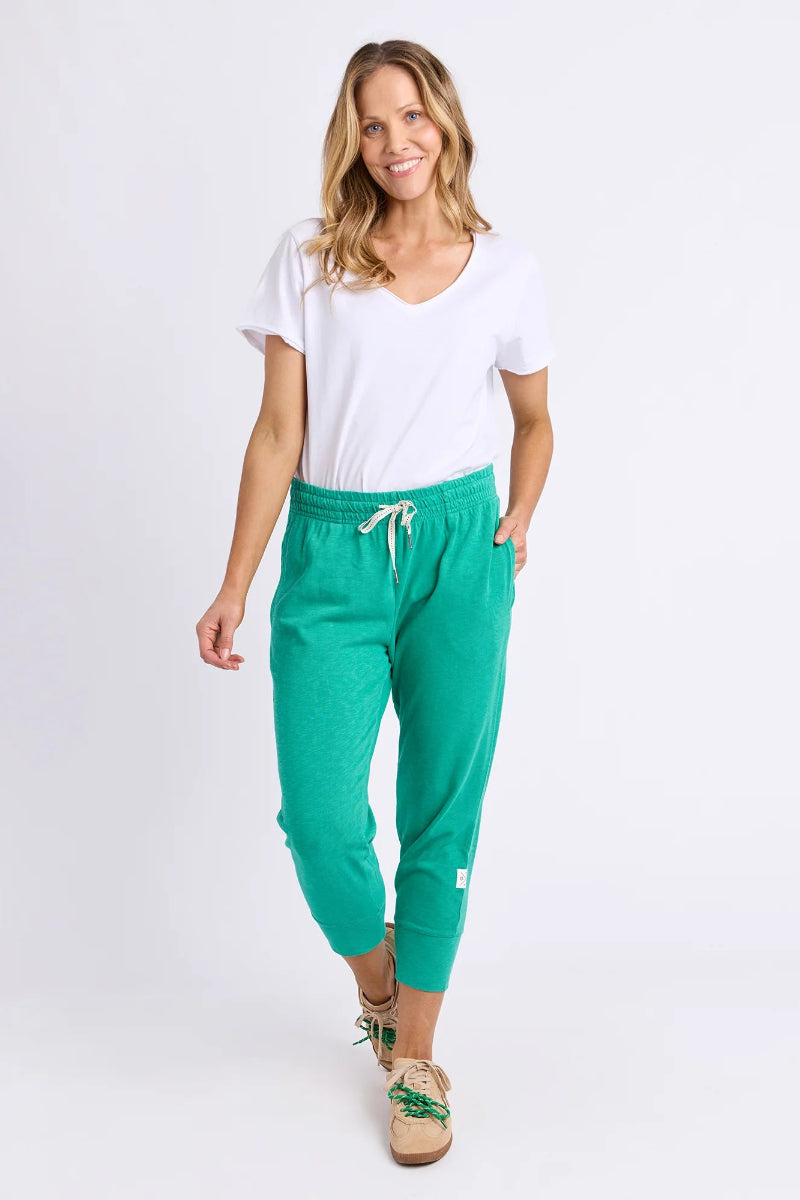 A woman modeling bright green jogger pants with a white drawstring, styled with a white t-shirt and tan lace-up sandals against a plain white studio background.