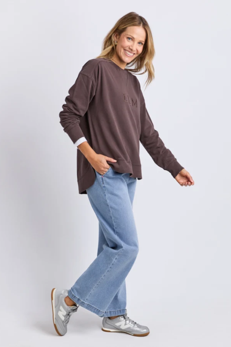 Woman wearing a brown oversized sweater and blue jeans on a white background