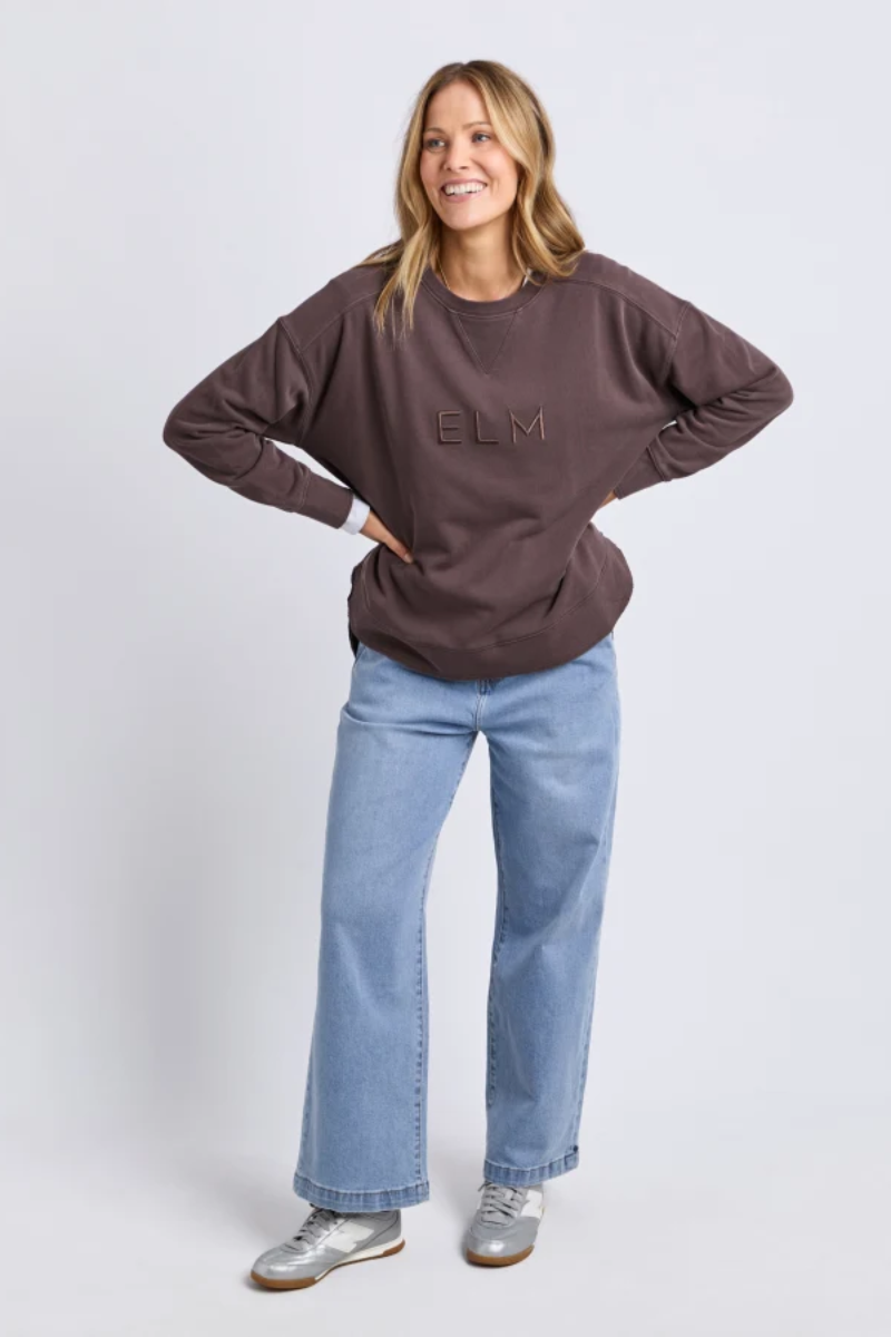 Woman wearing a brown sweatshirt with 'BLM' text and blue jeans on a white background