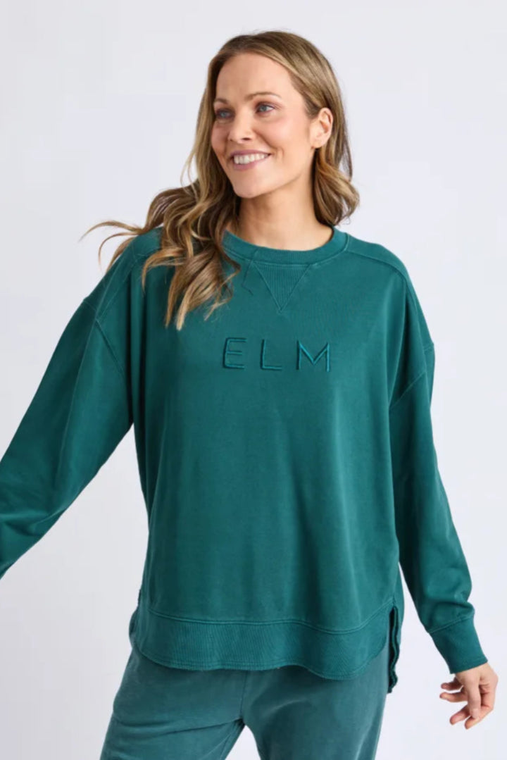 Woman wearing a teal sweatshirt with 'ELM' logo on a white background