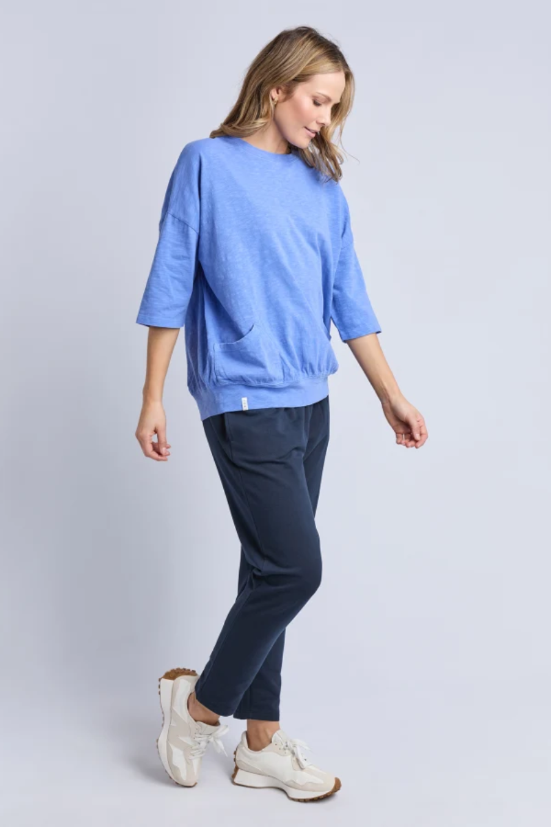 Woman wearing a blue top and navy pants on a light gray background