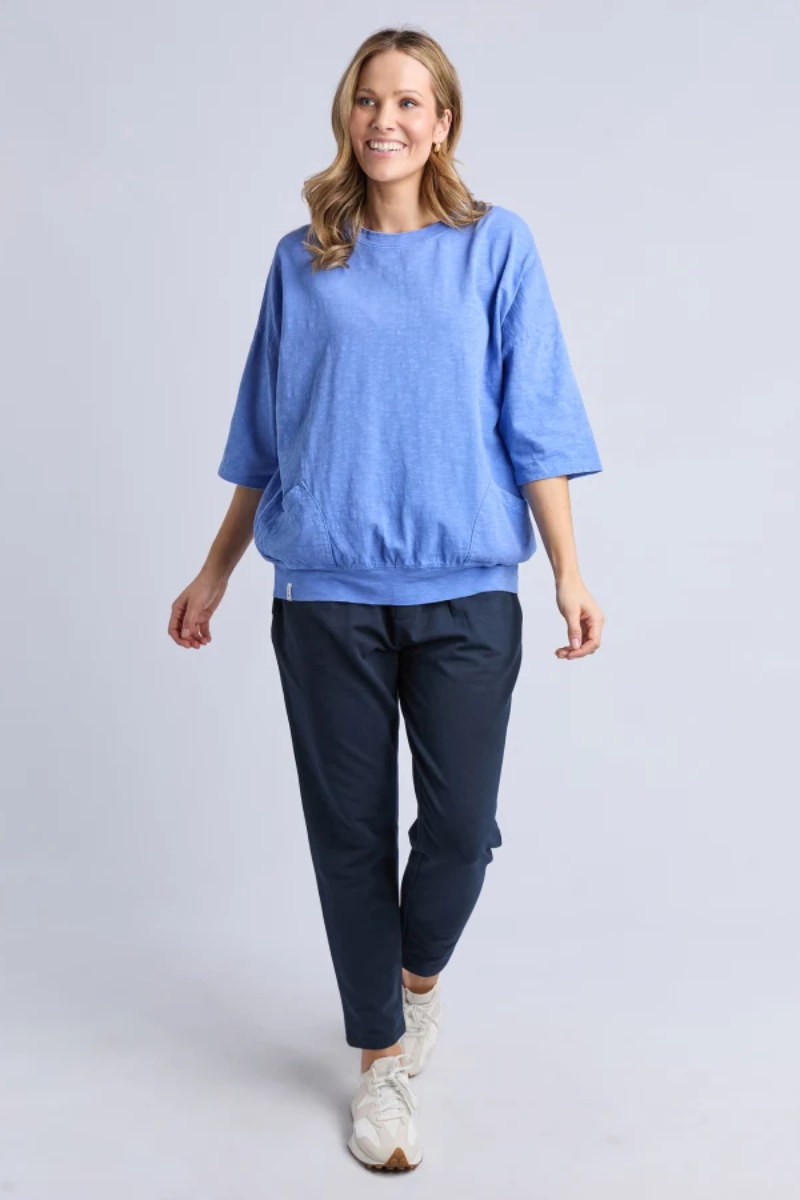 Woman wearing a blue top and dark pants on a light gray background