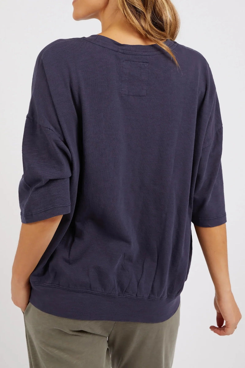 A woman shown from the back wearing a dark navy blue, relaxed-fit crewneck sweatshirt and olive green pants against a plain white background.