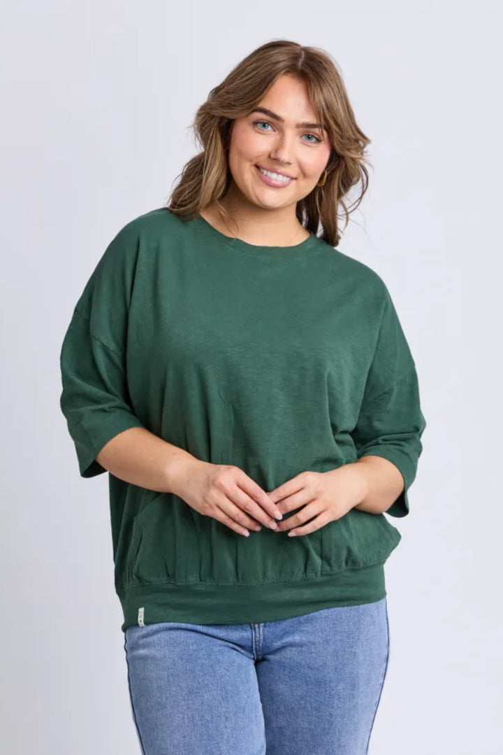Woman wearing a green sweater and blue jeans on a light gray background