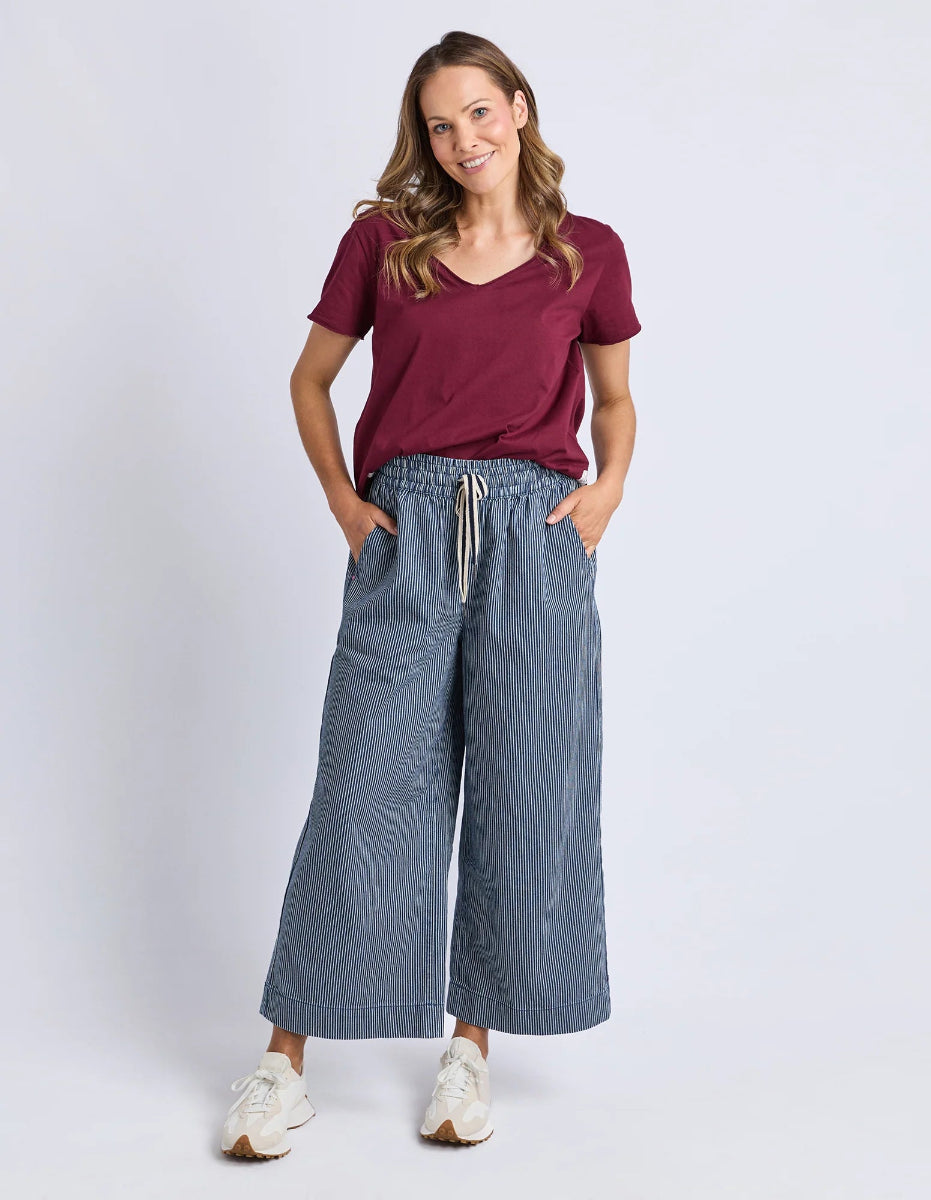 Woman wearing a maroon t-shirt and blue wide-leg pants on a white background