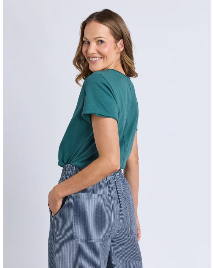 Woman wearing a teal top and blue striped pants on a light gray background