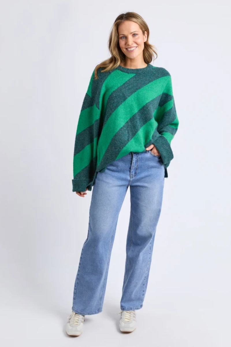 Woman wearing a green and black striped sweater with blue jeans on a white background