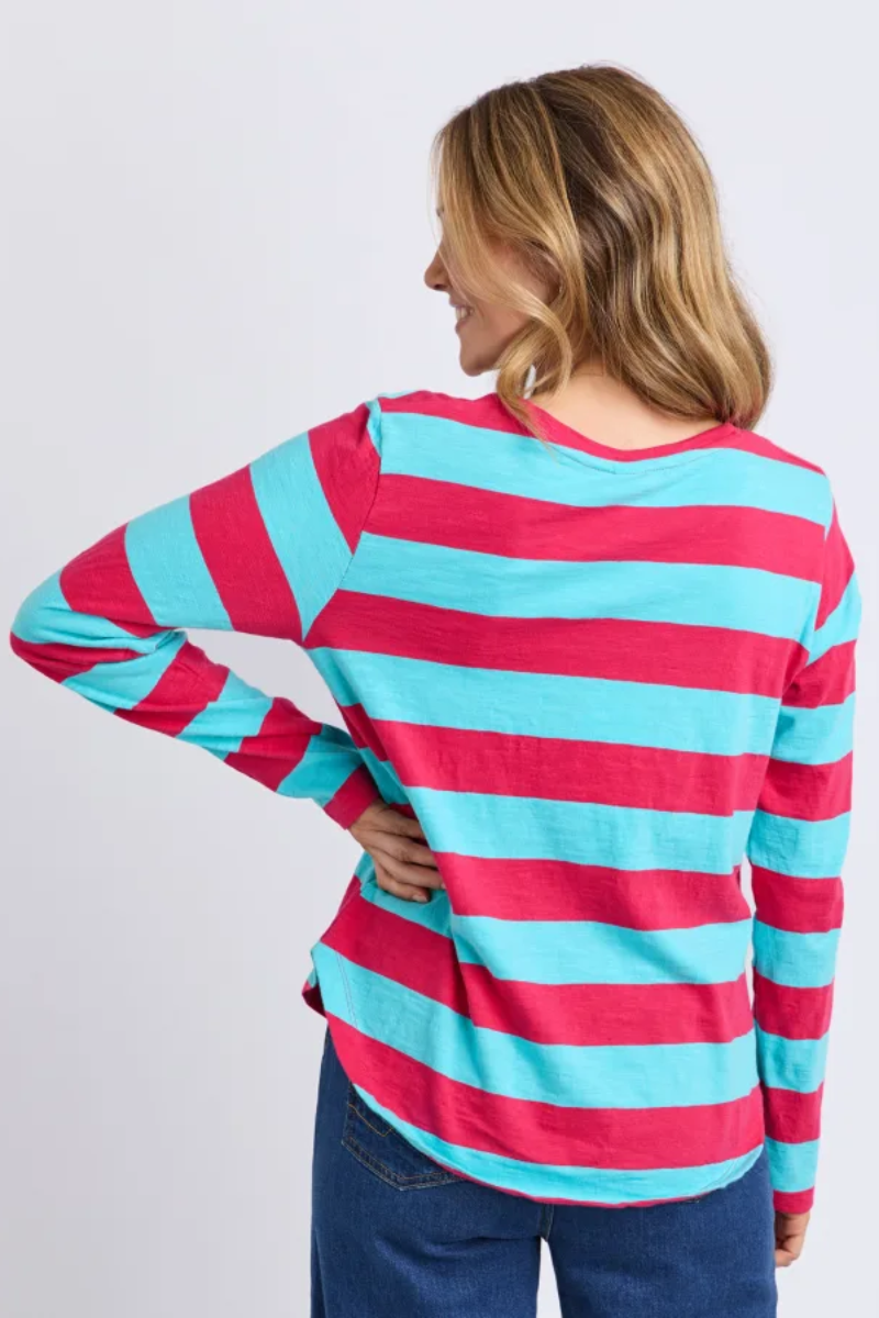 A woman wearing a long-sleeve striped shirt with alternating bright pink and turquoise horizontal stripes, shown from the back against a plain light gray background.