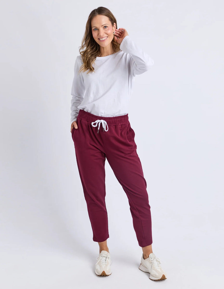 Woman wearing a white long-sleeve top and maroon jogger pants on a white background