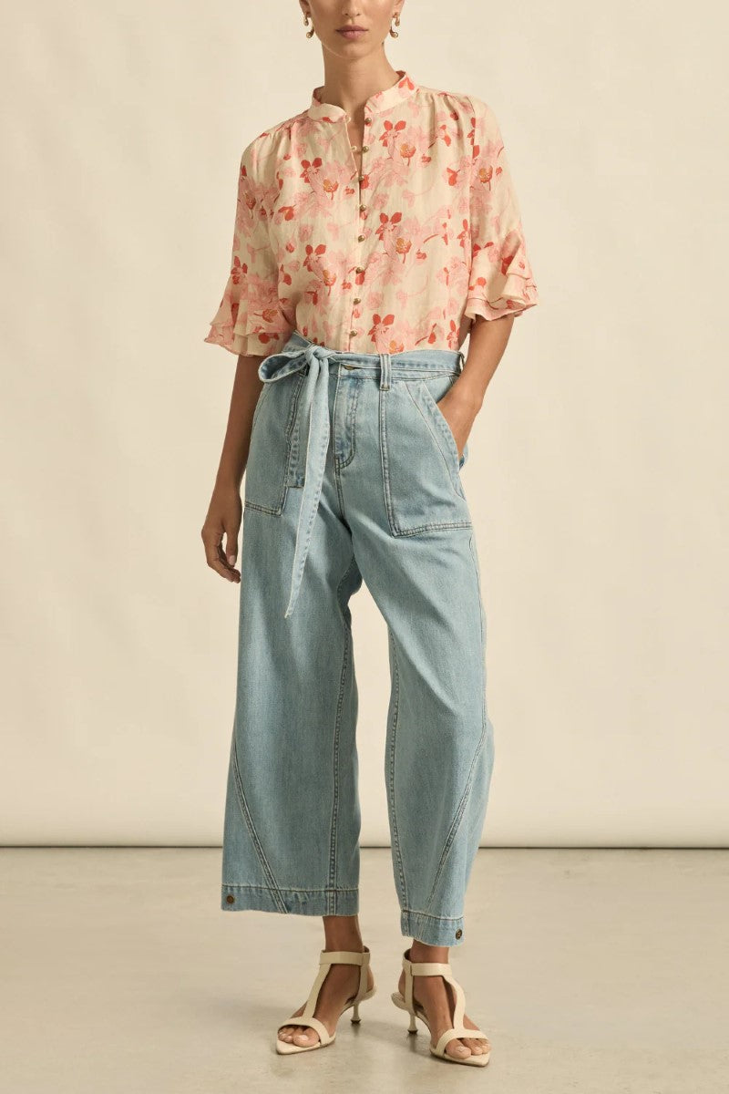 Person wearing a floral blouse and light blue pants on a neutral background