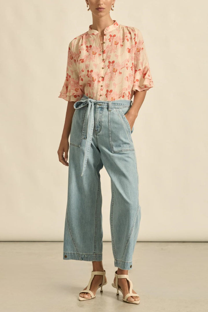 Person wearing a floral blouse and light blue pants on a neutral background
